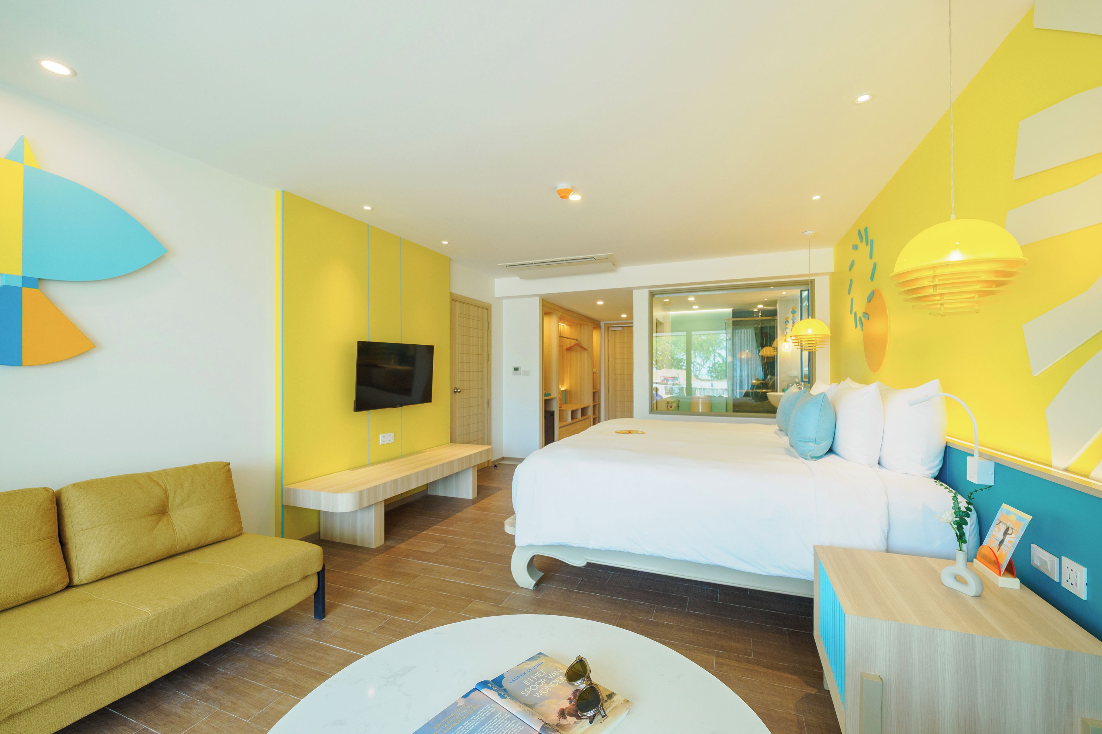 A modern hotel room with a bed, a sofa, a TV, and a dining area.