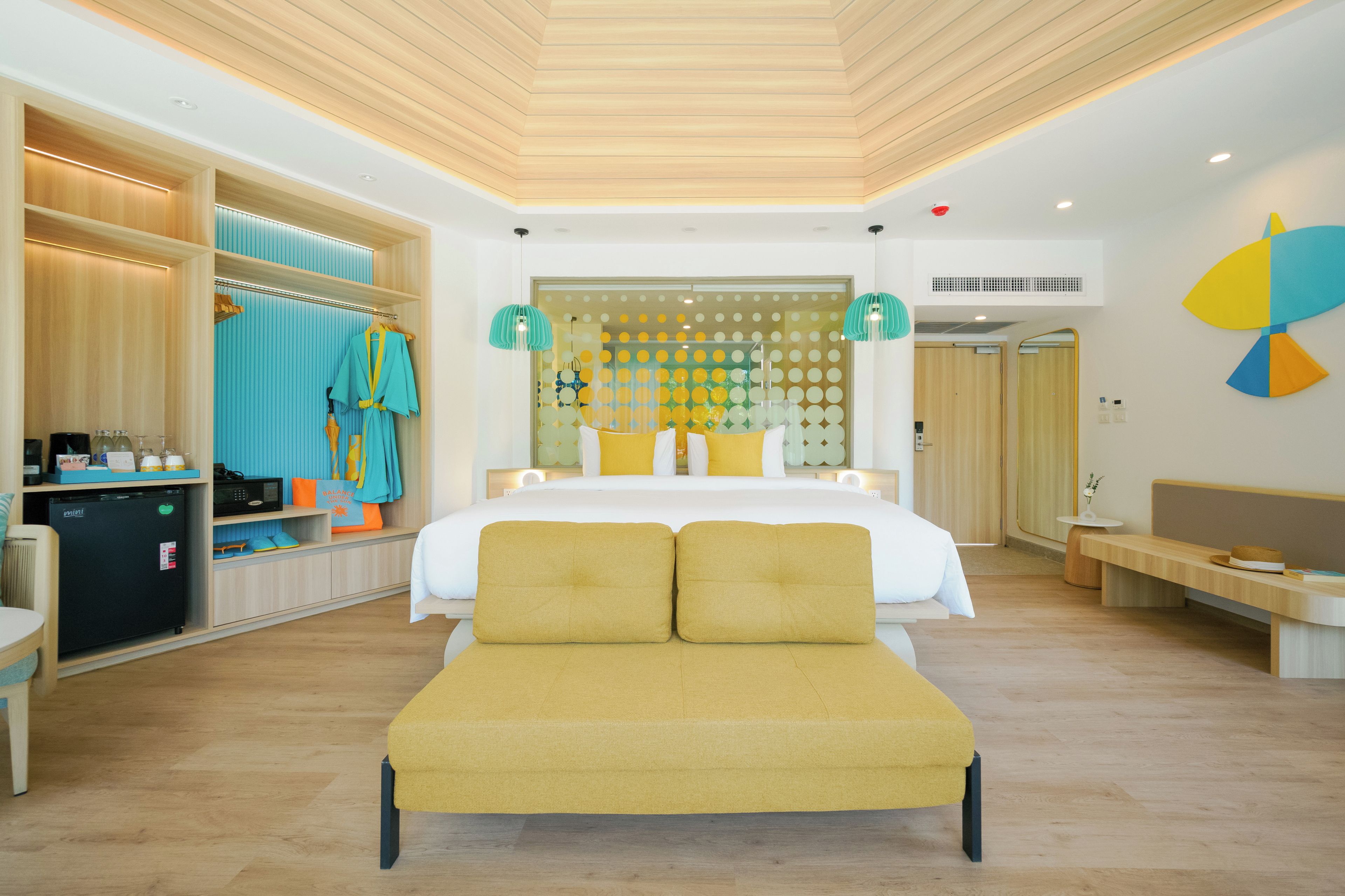 A modern hotel room with a bed, a seating area, a kitchenette, and a bathroom.