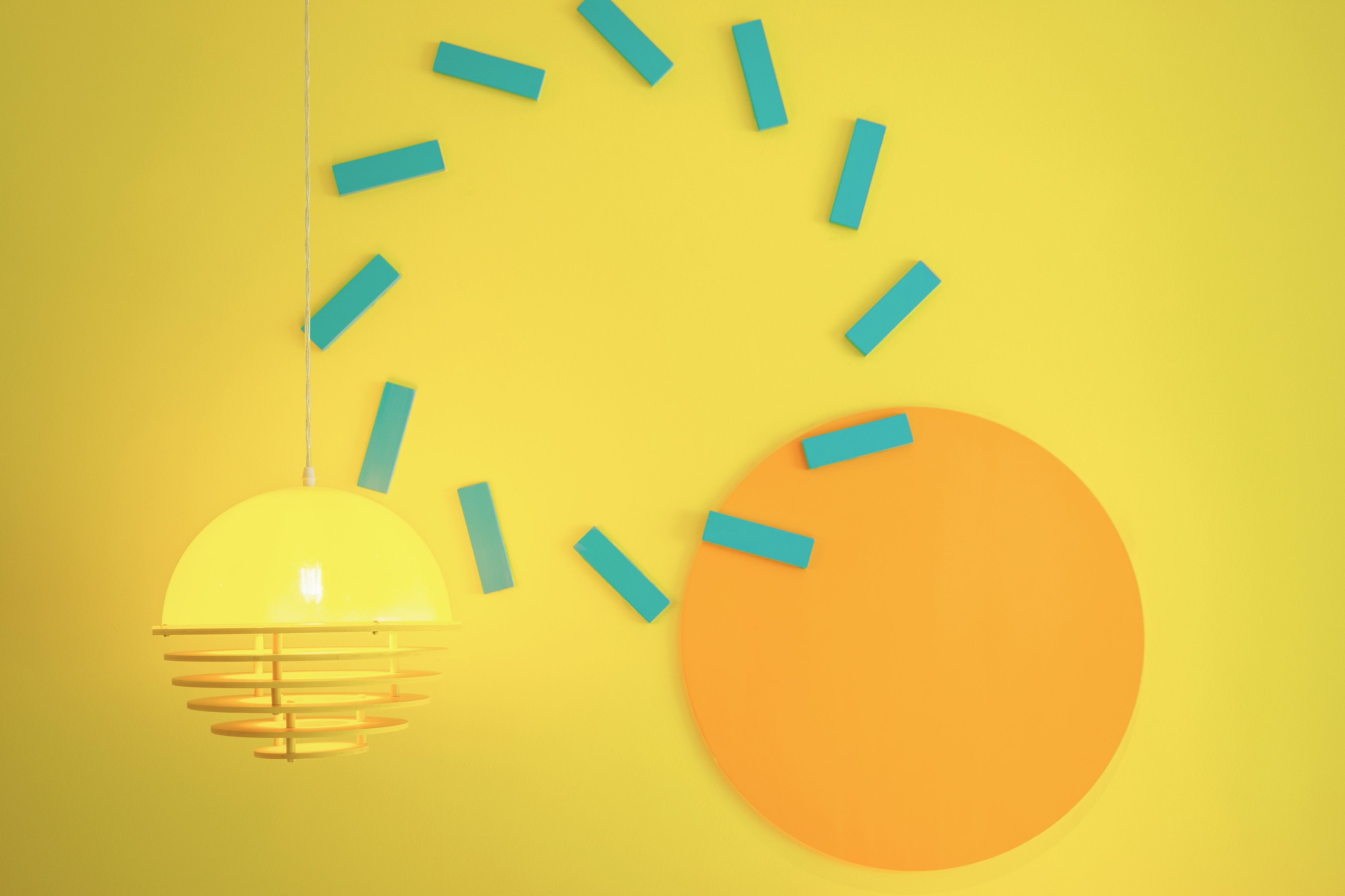 Un mur jaune orné d’une forme circulaire orange et d’un luminaire suspendu.