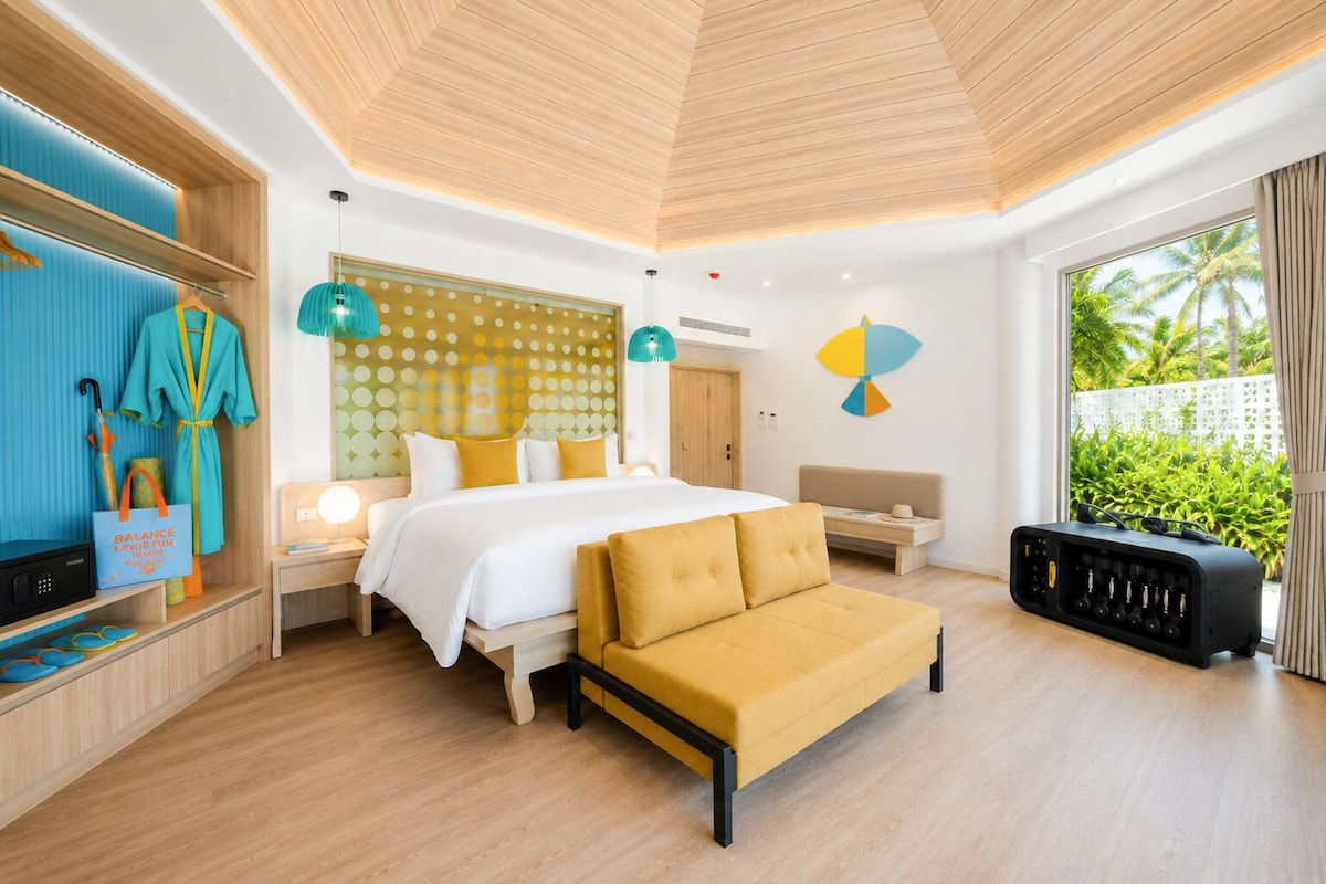 Een moderne hotelkamer met een bed, een slaapbank, een bureau en uitzicht op groen.