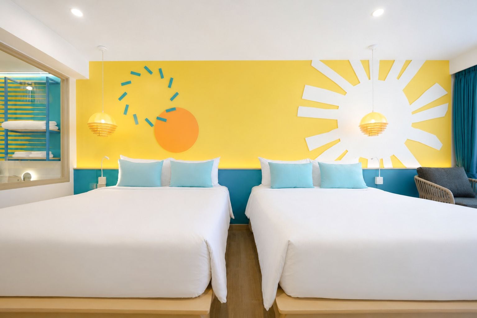 Habitación de hotel con dos camas, un gran mural con motivos de sol y vistas al mar.