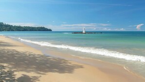 Una playa con un faro, cielo azul despejado y mar tranquilo.