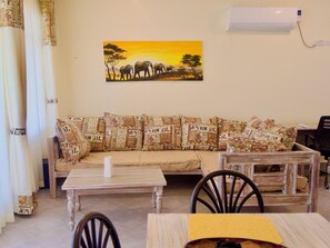 Un salon avec un canapé, deux tables et un tableau représentant des éléphants accroché au mur.