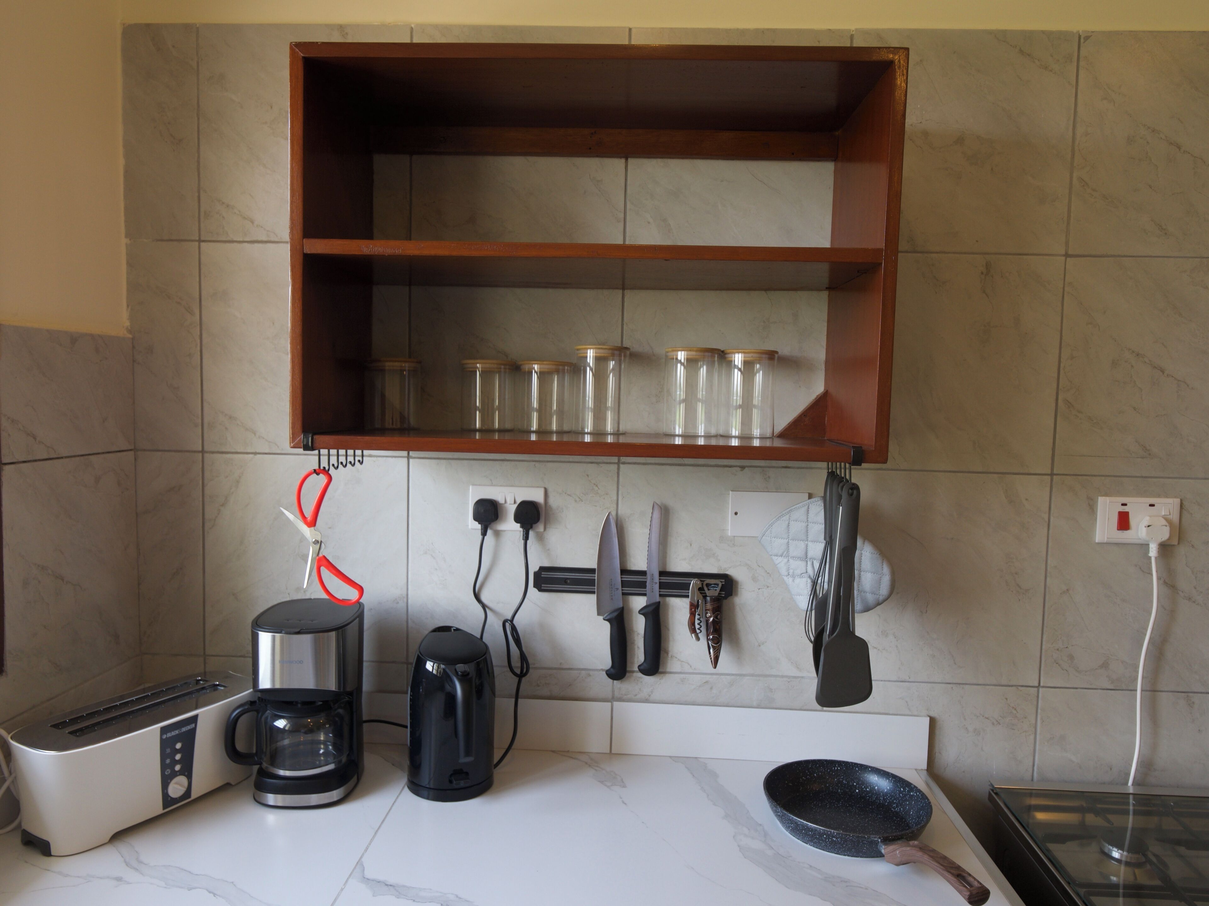 Une cuisine équipée d’un grille-pain, d’une machine à café et d’une poêle sur le plan de travail.