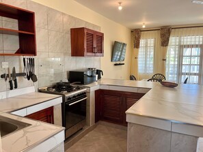 Una cocina con estufa a gas, horno y microondas, armarios de madera y una zona de comedor con mesa y sillas.