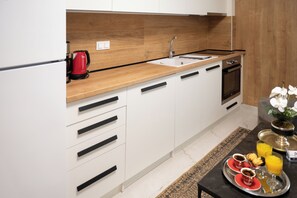 Eine moderne Küche mit weißen Schränken, einer Holz Arbeitsplatte, einem roten Wasserkocher, einer Spüle und einem Frühstücksbrett mit Kaffee, Gebäck und Orangensaft.