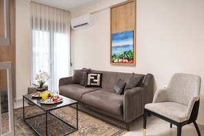 A living room with a sofa, a chair, a coffee table, and a painting on the wall. - Alexandra Boutique Residence Downtown  (Alexandroupoli)