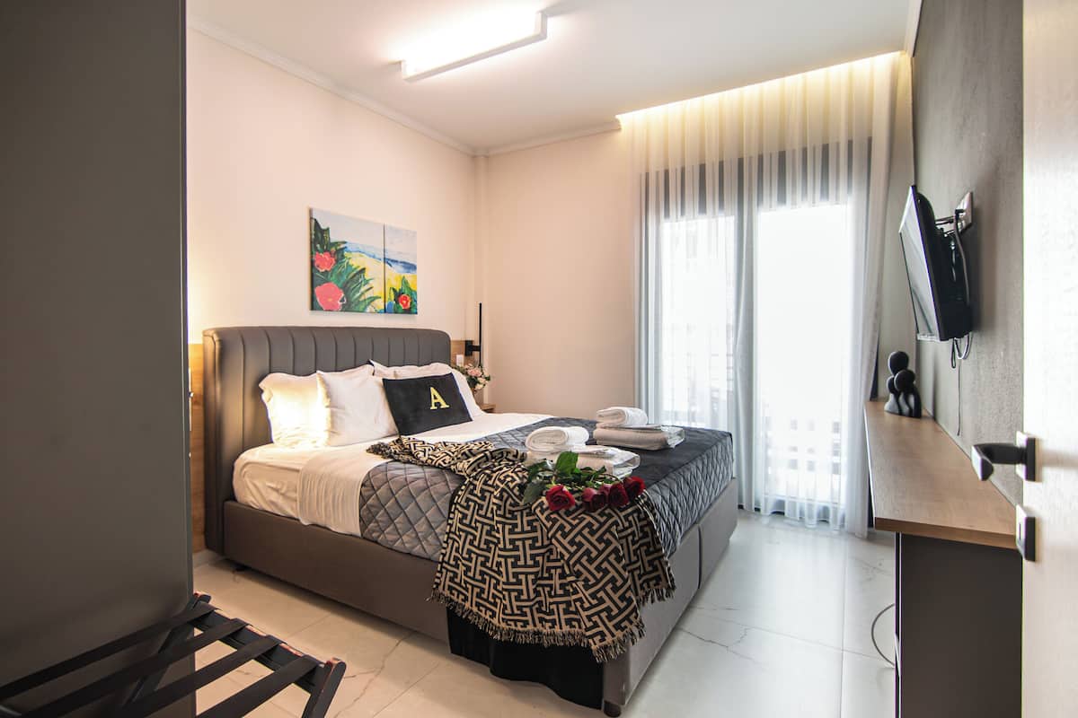 A modern hotel room with a bed, a flat-screen TV mounted on the wall, and a window with curtains.