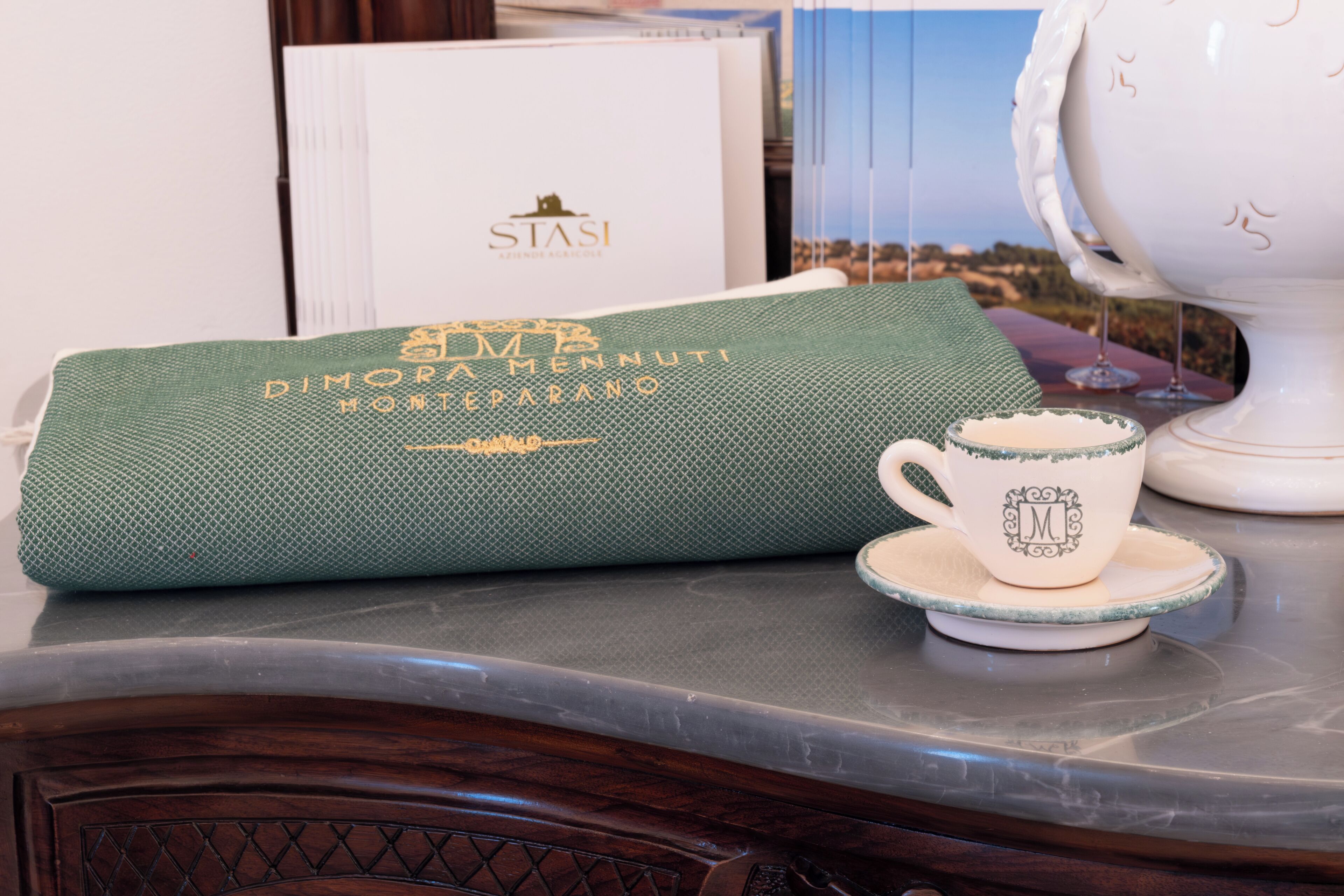 Una mesa servida con una servilleta verde, una taza blanca con un monograma y una tetera blanca.