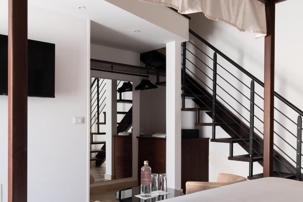 Una habitación moderna con una cama, una mesa con una botella y vasos, un televisor y una escalera.