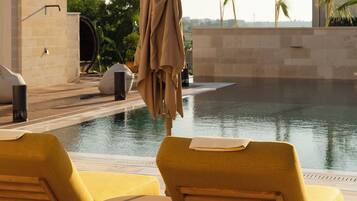 A poolside area with lounge chairs and a covered umbrella, a water feature, and a view of the surrounding landscape.