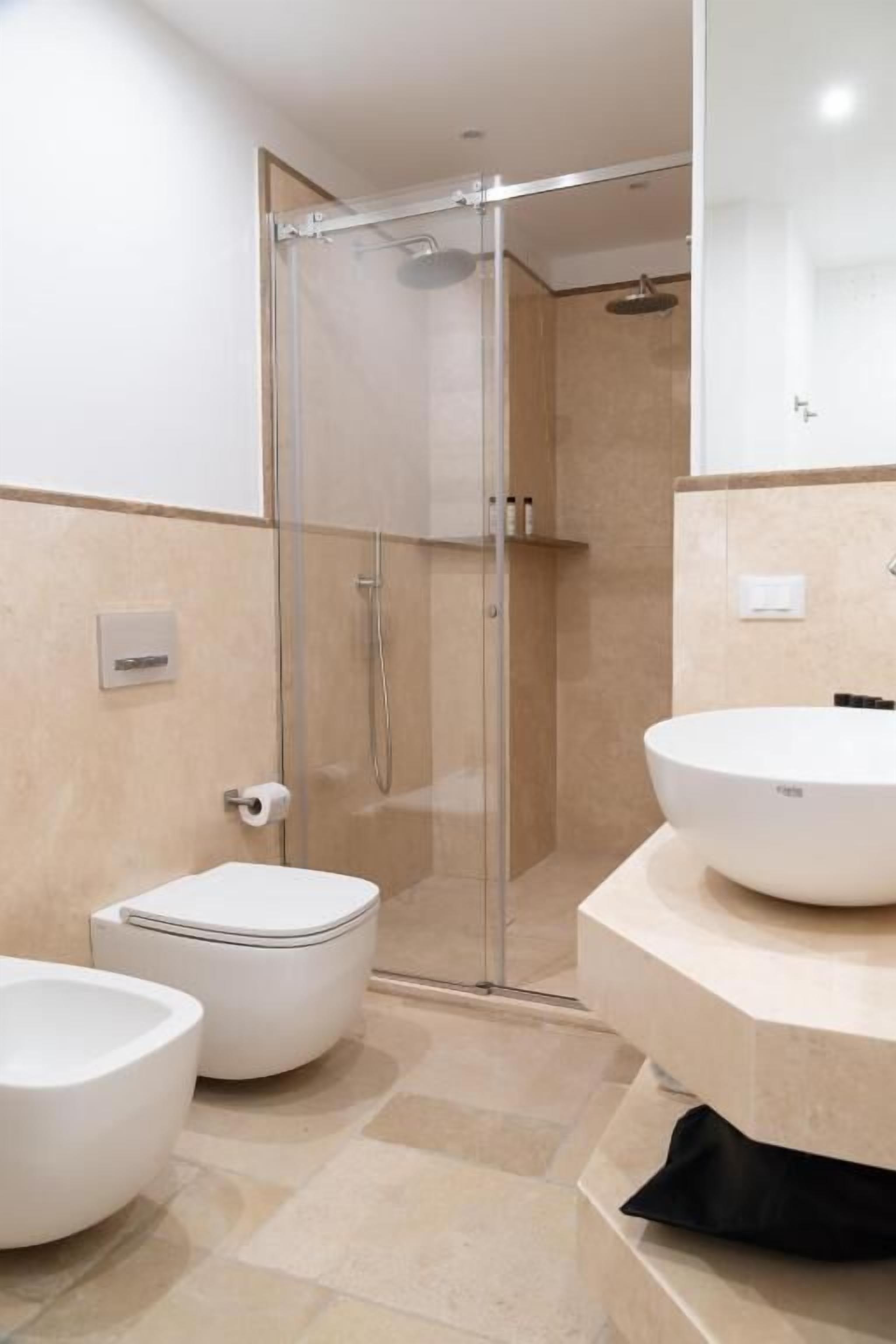 A modern bathroom with a glass-enclosed shower, a white sink, and a bidet.