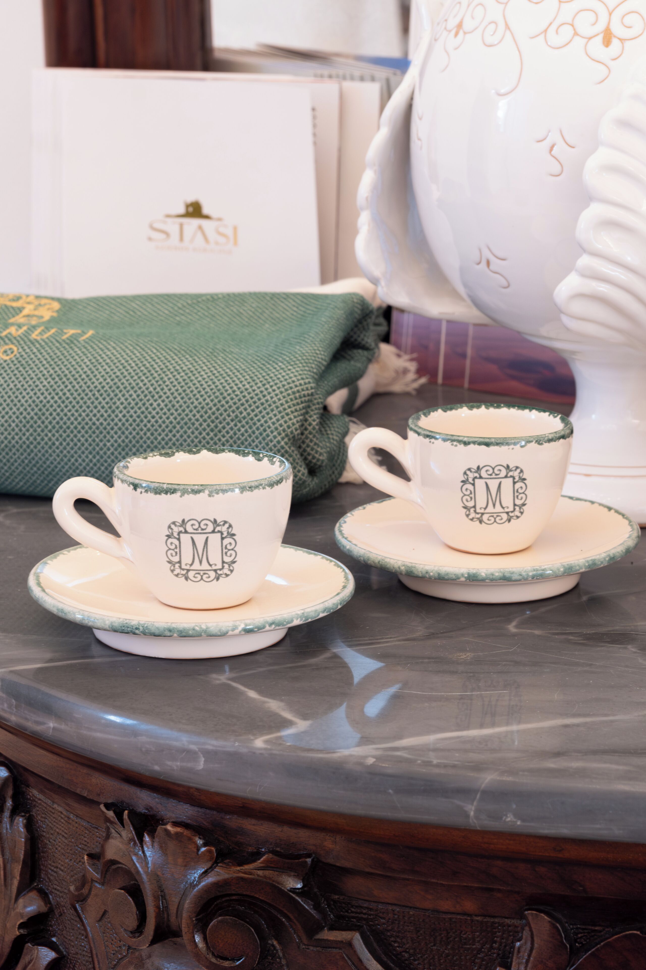 A table with two matching cups and saucers, a green cushion, and a white box with 'STASI' branding.