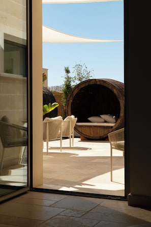 Un interior moderno con una cama de barril de madera grande, sillas de mimbre blanco y una puerta de cristal que da a un patio exterior.