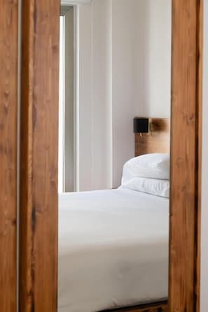 A bedroom with a wooden headboard, white bedding, and a visible door frame.