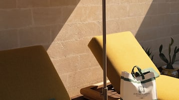 Ein sonniger Außenbereich mit Sitzgelegenheiten, einem Tisch, einem Liegestuhl und einem kleinen runden Tisch.