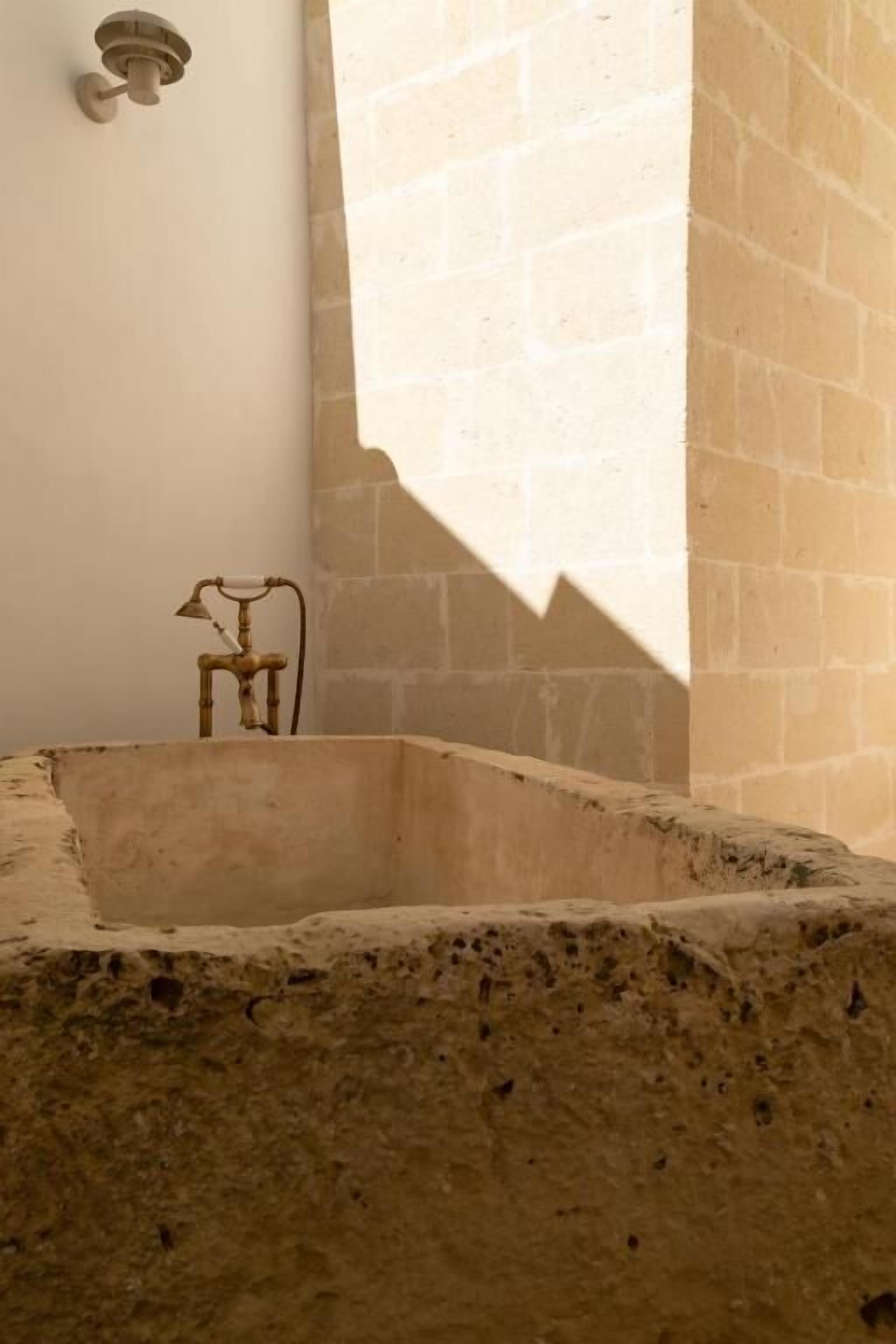 A stone bathtub with a faucet, a wall-mounted light fixture, and a shadow cast by a window.