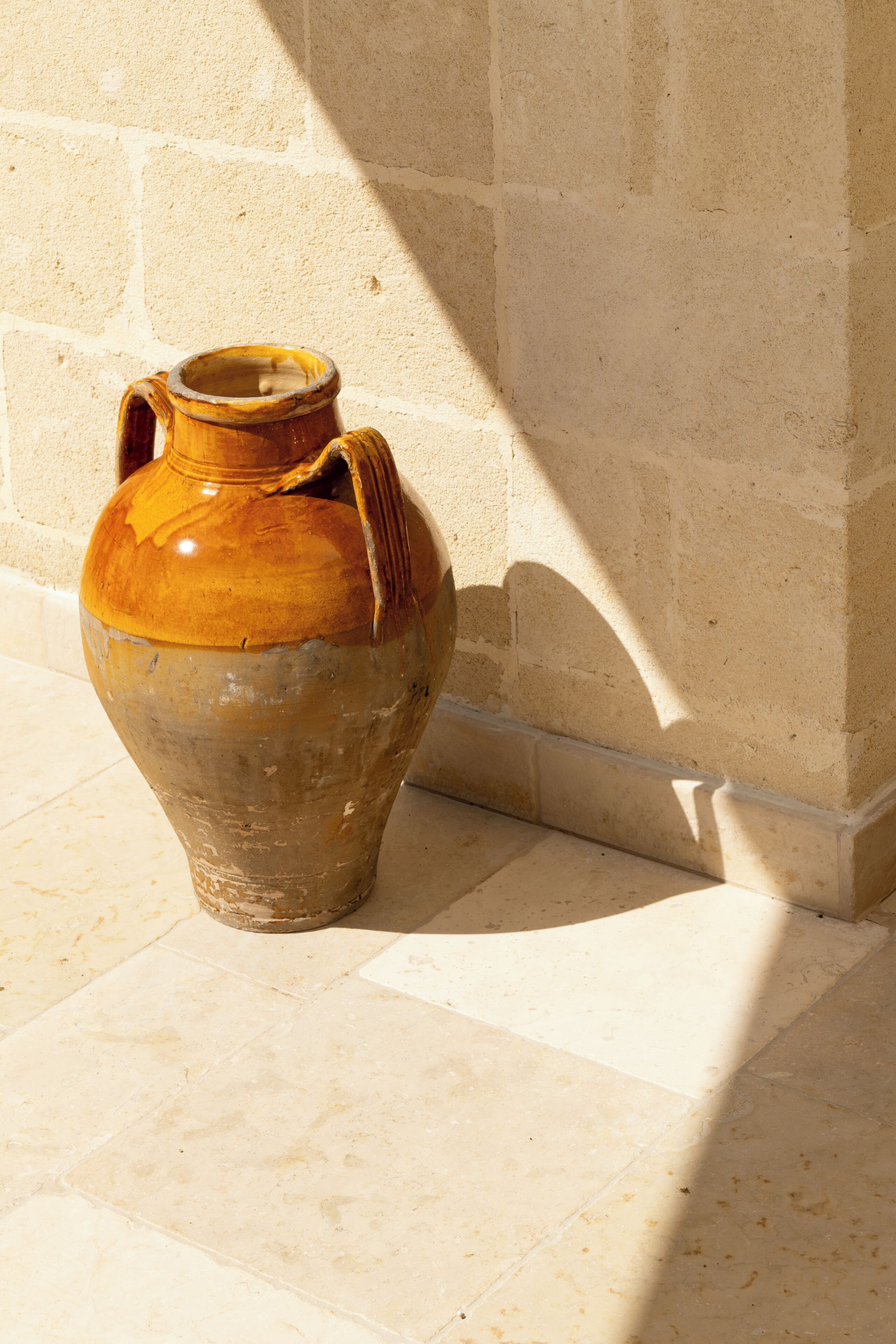 A large ceramic jug against a wall with a shadow cast on the floor.