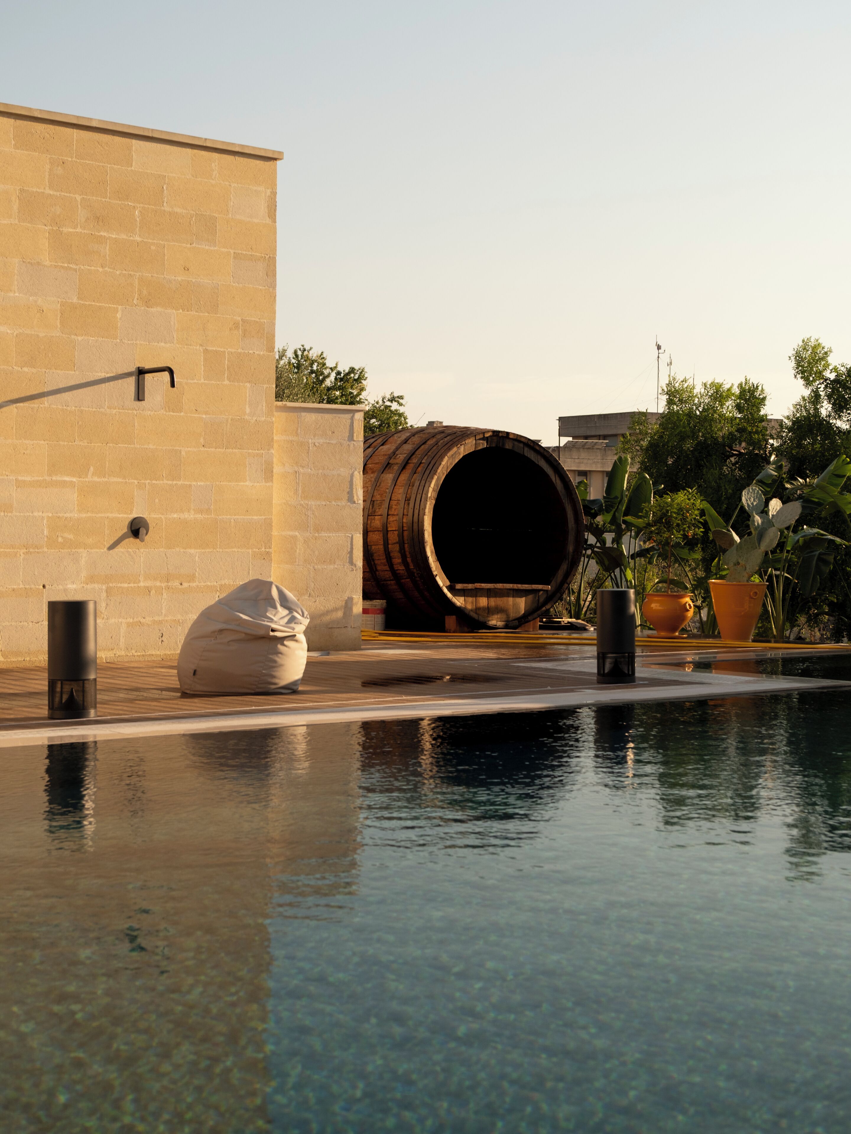 Piscina com um barril, parede bege e plantas em vasos.