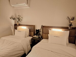 Ett hotellrum med två sängar, var och en med en kudde märkt med texten ”HOTEL Amy”, ett sängbord med en bok och en dekorativ prydnad samt en väggmonterad luftkonditioneringsanläggning.