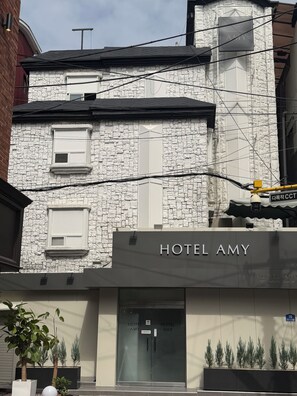 En byggnad med en fasad av sten, en skylt med texten ”HOTEL AMY” och en modern entré med en glasdörr.