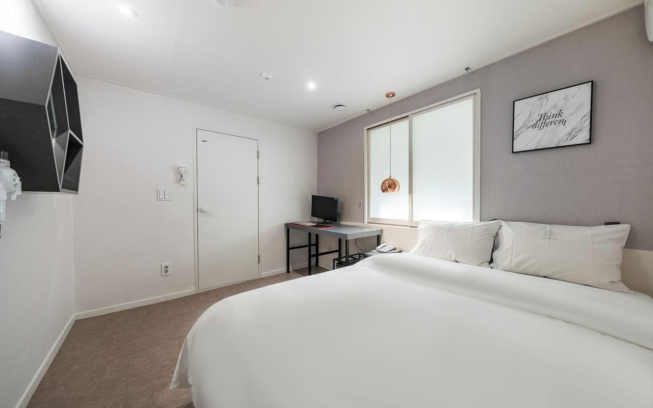 Habitació d'hotel moderna amb un llit gran, una taula de treball amb un ordinador, una televisió i una finestra ampla.