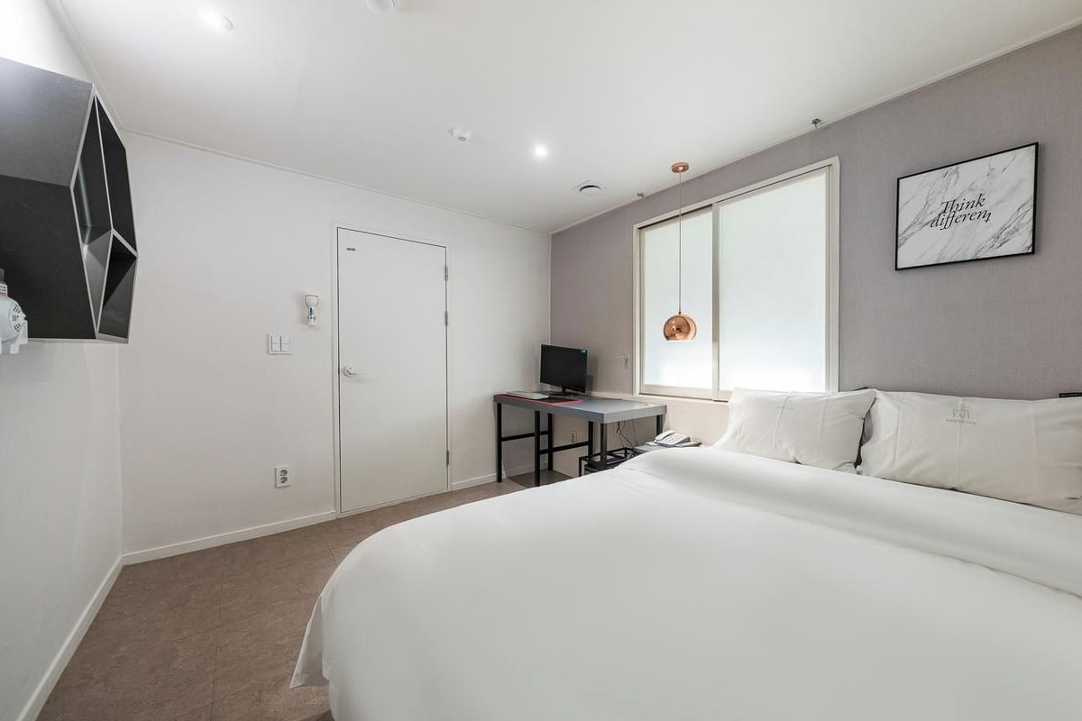 Una habitación de hotel moderna con una cama grande, un escritorio con ordenador, una televisión y un ventanal amplio.