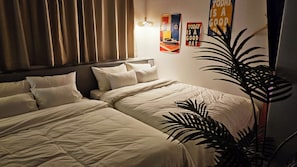 Habitació d'hotel amb dos llits, una planta gran en test i pòsters motivacionals a la paret.