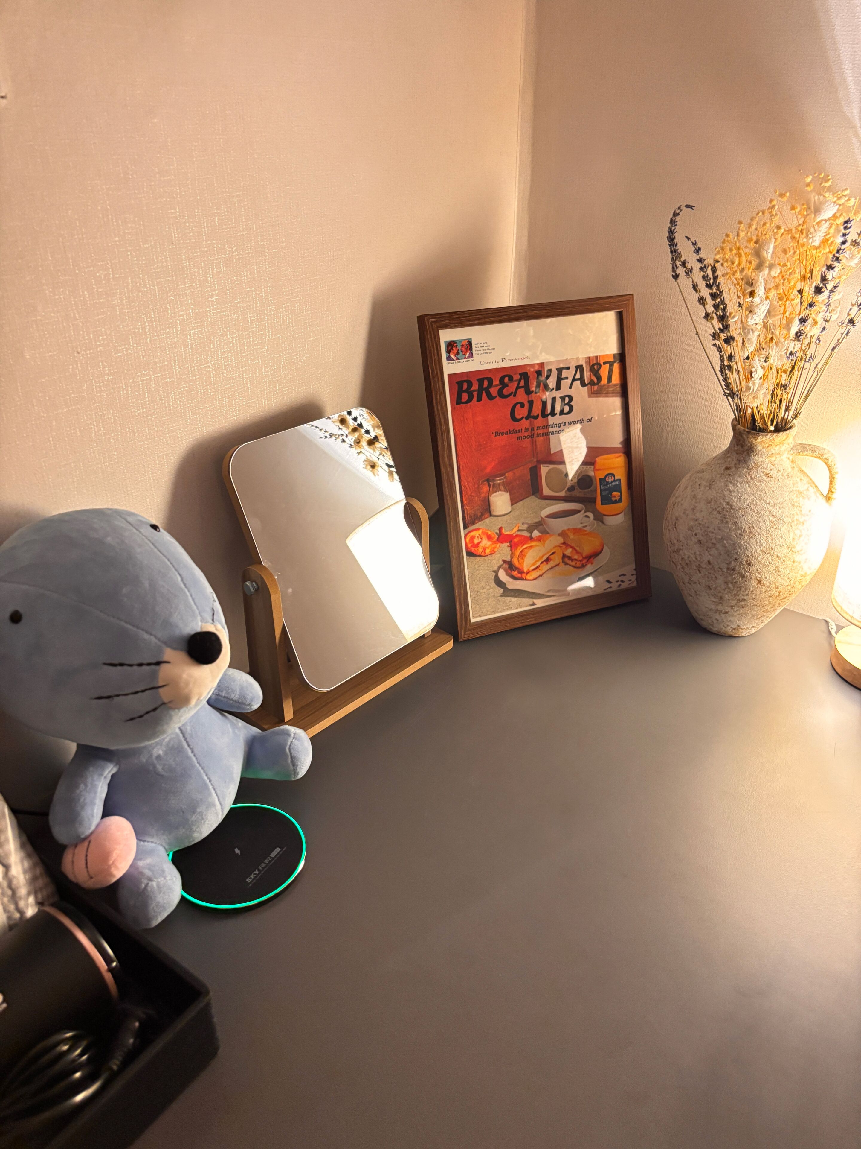 A room with a framed poster, a plush toy, and a vase with dried flowers.