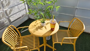 Mesa e cadeiras amarelas ao ar livre, com um vaso de planta e uma bebida sobre a mesa.