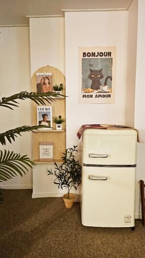 Una habitación de estilo vintage con un refrigerador blanco, un armario de madera, una planta en maceta y un cartel en la pared.