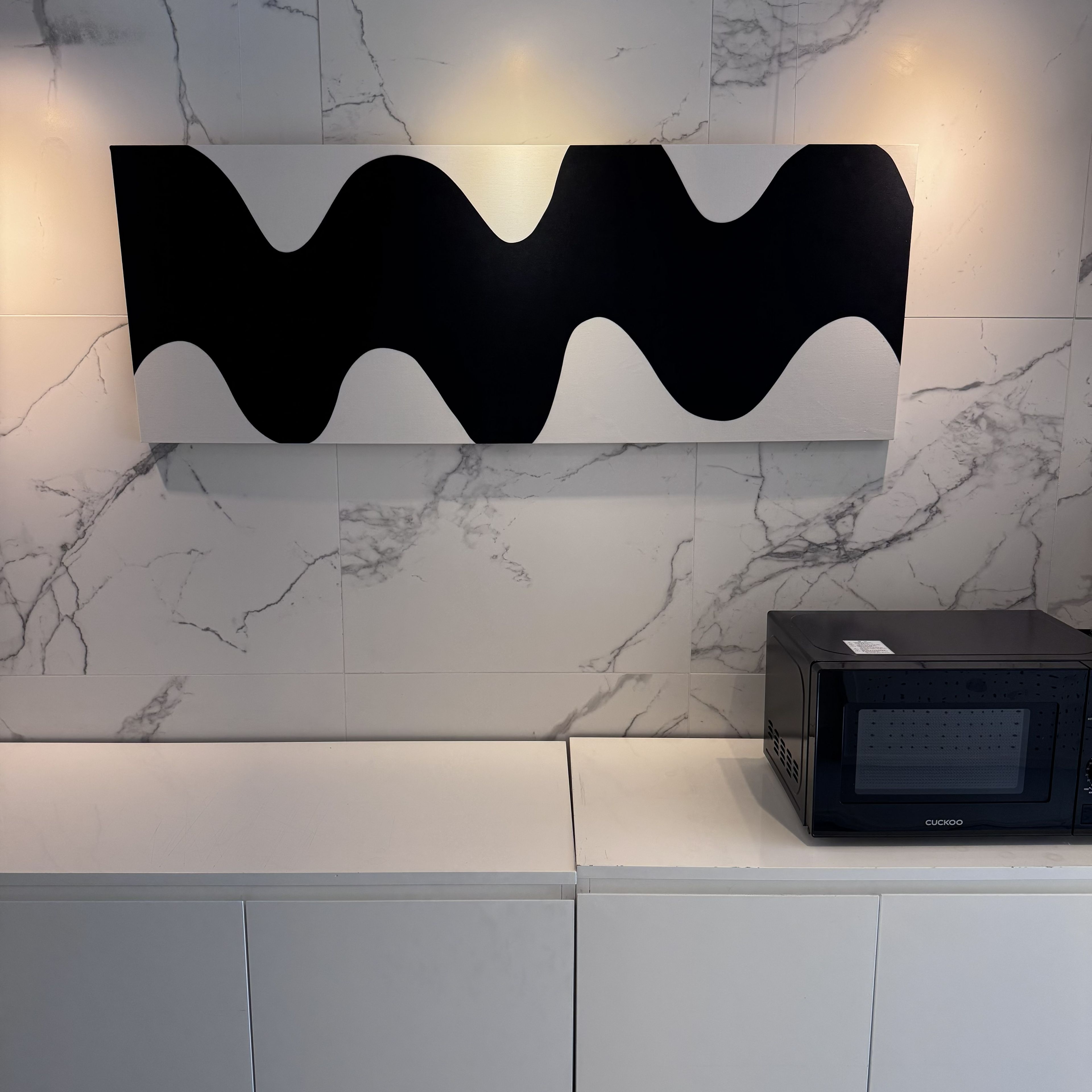 A kitchen with a marble backsplash, a black microwave, and a black and white abstract wall art piece.