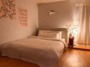Un dormitori amb un llit, una làmpada penjada a la paret, una finestra amb cortines i una decoració mural amb text.