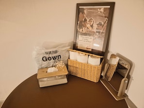 Una habitación con un cuadro enmarcado, una cesta de mimbre, una caja de pañuelos y una bolsa con la etiqueta 'Gown'.