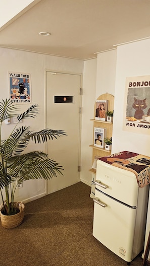A corner room with a white door, a vintage refrigerator, a potted plant, and wall decorations including a 'Wash Your Little Paws' sign and a 'Bonjour Mon Amour' poster. - Hotel Amy (Incheon)