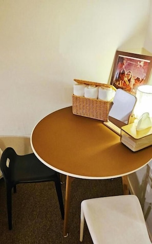 Una mesa redonda con una cesta de mimbre que contiene toallas enrolladas, una silla blanca, una pequeña mesa blanca y un cuadro enmarcado.