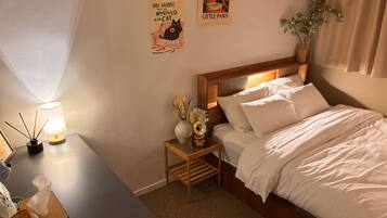 A neatly arranged bedroom with a bed, bedside tables, a lamp, a small decorative vase, and a wall poster.