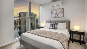Une chambre moderne avec un grand lit, deux tables de chevet avec des lampes, une vue sur la ville et un appareil de climatisation.