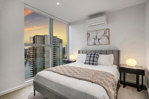 Ein modernes Schlafzimmer mit einem großen Bett, zwei Nachttischen mit Lampen, Blick auf die Stadt und einer Klimaanlage.
