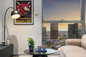 Ein modernes Wohnzimmer mit Stadtblick, einem gerahmten Poster, einem Tisch mit Büchern und einer Pflanze sowie einer Lampe.