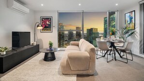 Un salon moderne comprenant un canapé, une table à manger et des chaises, un téléviseur à écran plat et une vue sur la ville grâce à de grandes fenêtres.