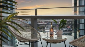 Un balcon avec des fauteuils en osier, une table en verre, une bouteille et des verres.