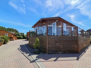 A wooden cabin with a balcony, a paved driveway, and a small garden area. - Banksy's Retreat (Ilfracombe)