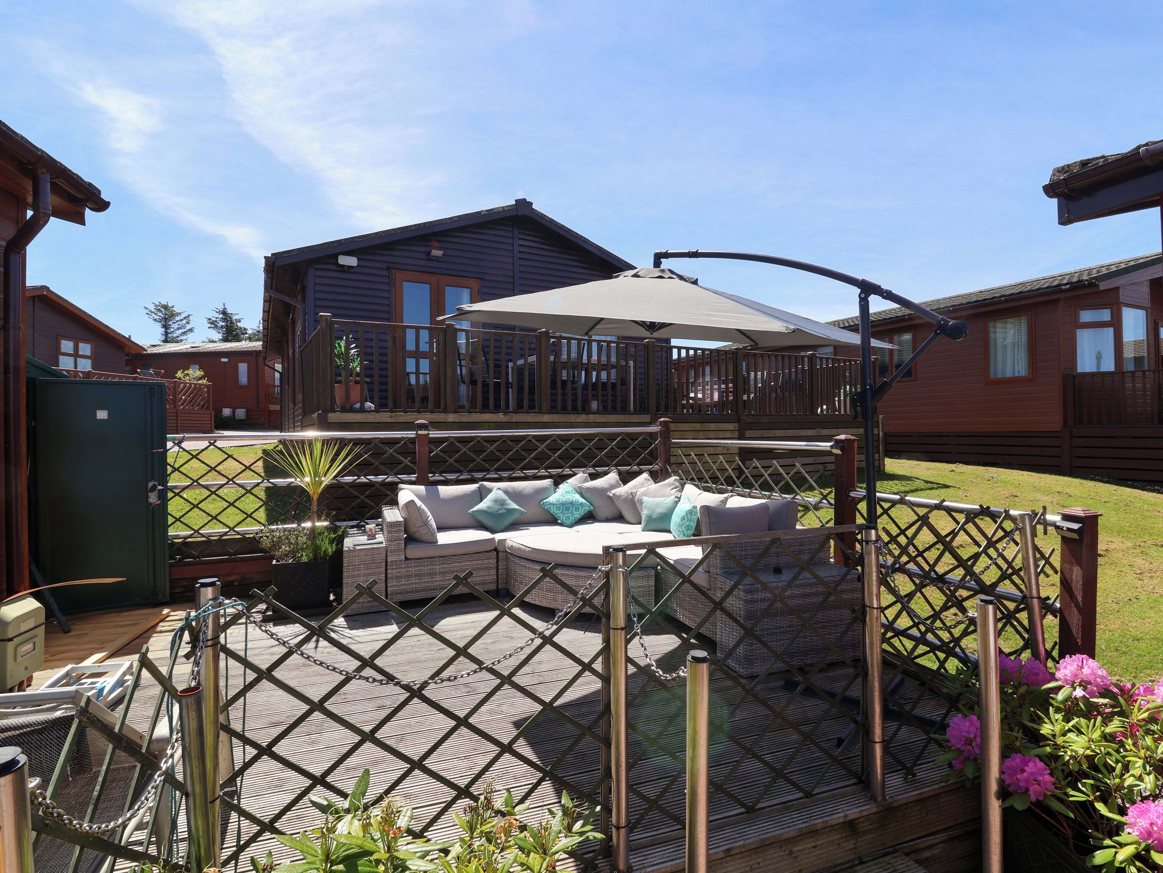 A covered outdoor seating area with a wooden deck, a cushioned sofa, and a pergola with a canopy.