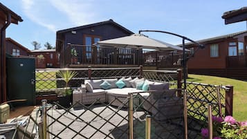 A covered outdoor seating area with a wooden deck, a cushioned sofa, and a pergola with a canopy.