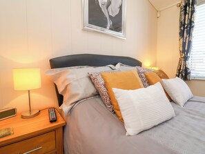 Una cama bien hecha con almohadillas estampadas, una lámpara de noche, un control remoto y un cuadro en la pared.