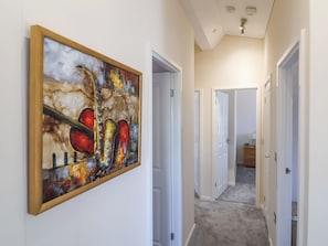 A hallway with a painting, white doors, and a carpeted floor.