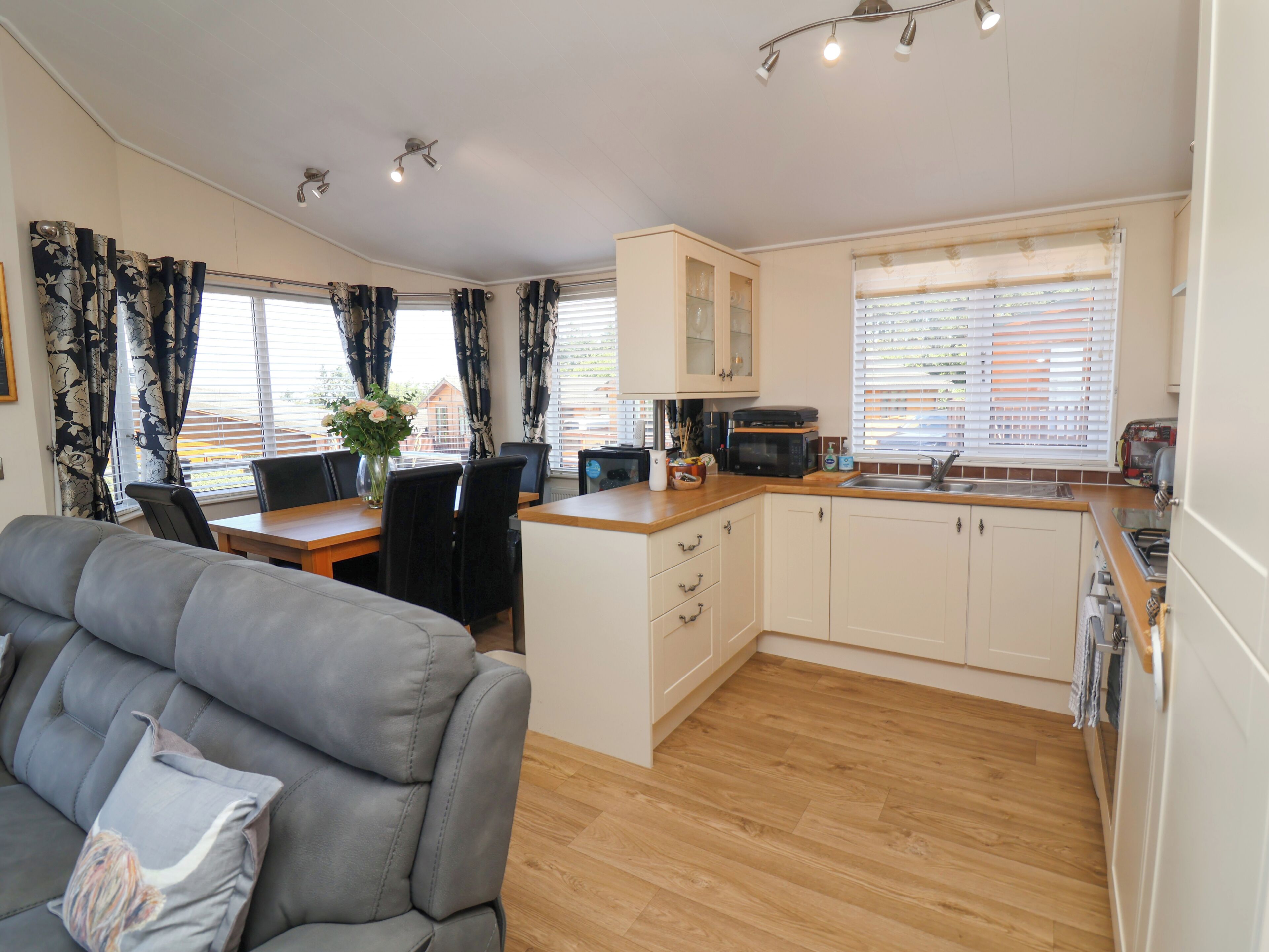 A compact living space with a sofa, dining table, chairs, a kitchen area with cabinets and appliances, and a window with blinds.