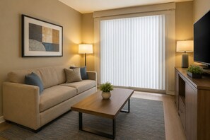 Ein modernes Wohnzimmer mit einer Couch, einem Couchtisch, einem Fernseher und einem großen Fenster mit Jalousien.