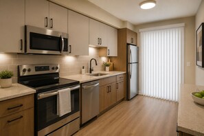 Eine moderne Küche mit Edelstahlgeräten, Holzschränken und einem großen Fenster mit Jalousien.